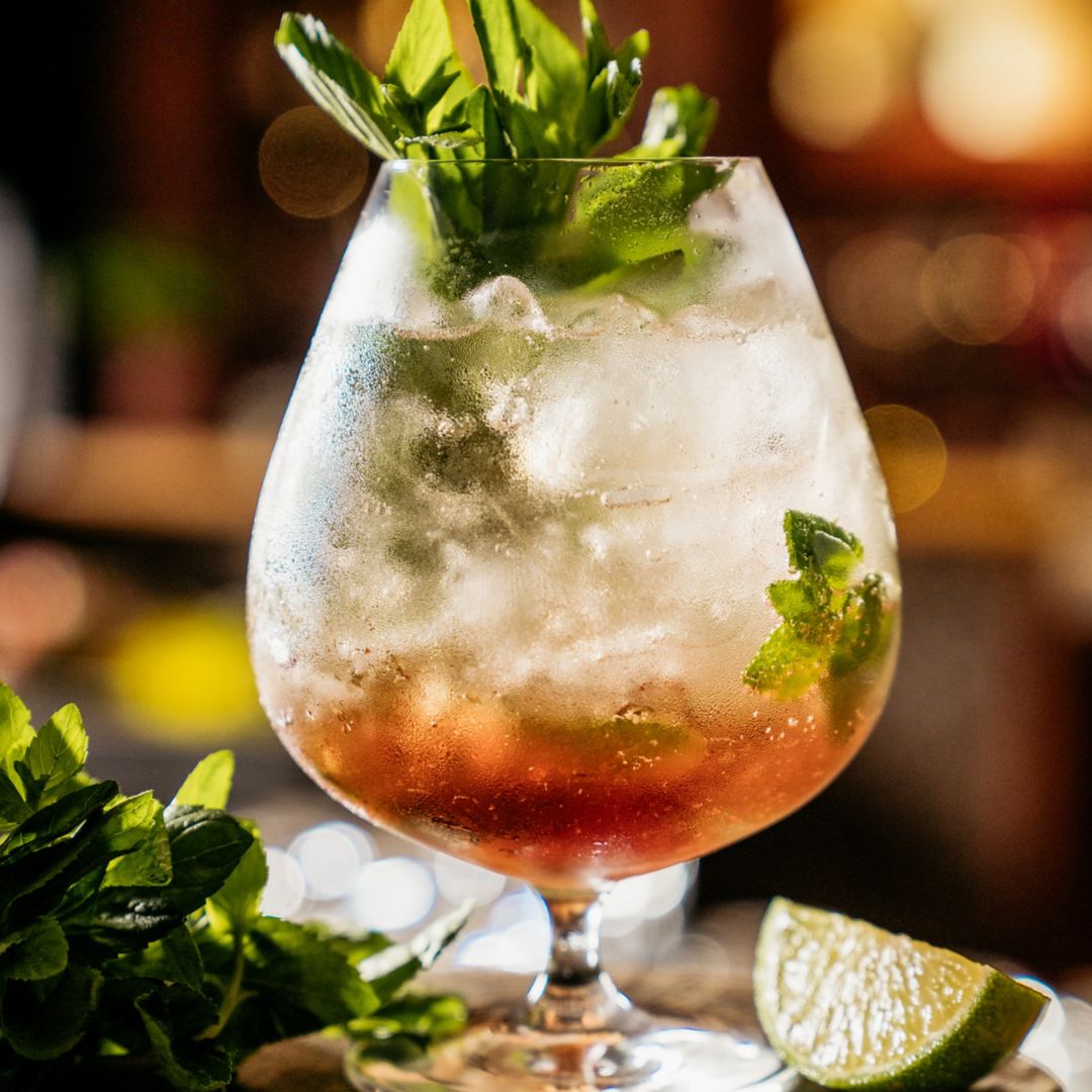 Zapote cocktail in a short stem wine glass, with mint garnish and lime